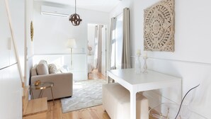 A modern living room with a white sofa, a glass coffee table, and a white dining table.