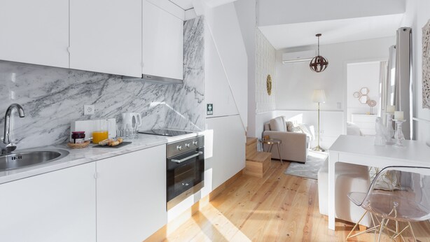 A modern kitchen with white cabinets, a marble countertop, and a wooden floor.