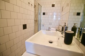 A modern bathroom with white tiles, a large sink, and a glass shower enclosure.