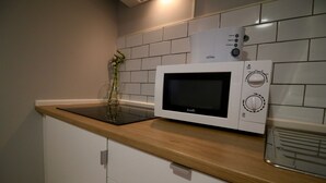 A kitchen with a microwave on a wooden countertop, a vase with a plant, and white tiled walls.