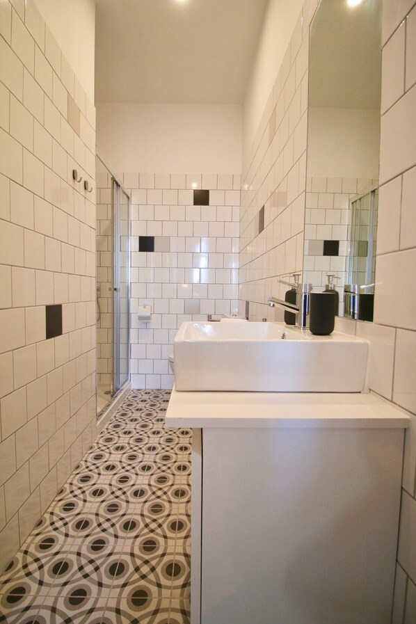 A modern bathroom with white tiles, a large mirror, a white sink, and a patterned floor.