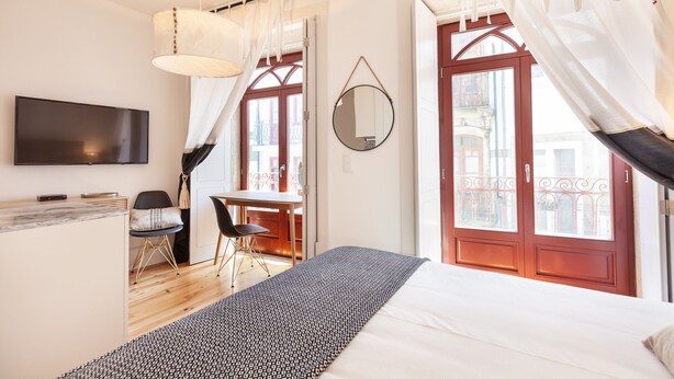 Ett modernt hotellrum med en säng, ett skrivbord, en stol, en TV och stora fönster med gardiner.