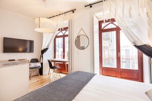 A modern hotel room with a bed, a desk, a chair, a TV, and large windows with curtains. - D&S - Falling Leaves (Oporto)