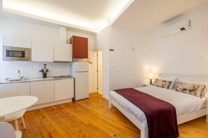 A compact hotel room with a kitchenette, a bed with a red blanket, and a bedside table. - TRY OPORTO - Ponte do Infante (Oporto)