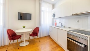 A modern kitchen with white cabinets, a microwave, a sink, and a built-in oven. There is a small round table with two red chairs and a flat-screen TV mounted on the wall. - TRY OPORTO - Ponte Dom Luís (Oporto)