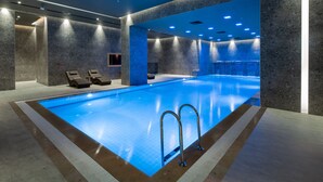 Una piscina interior moderna con agua azul cristalina, sillas de descanso y un diseño de pared de piedra.