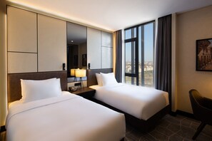 A hotel room with two beds, a large window with curtains, a desk with a lamp, and a chair. - Bureau Collection Hotel  (Kartepe)