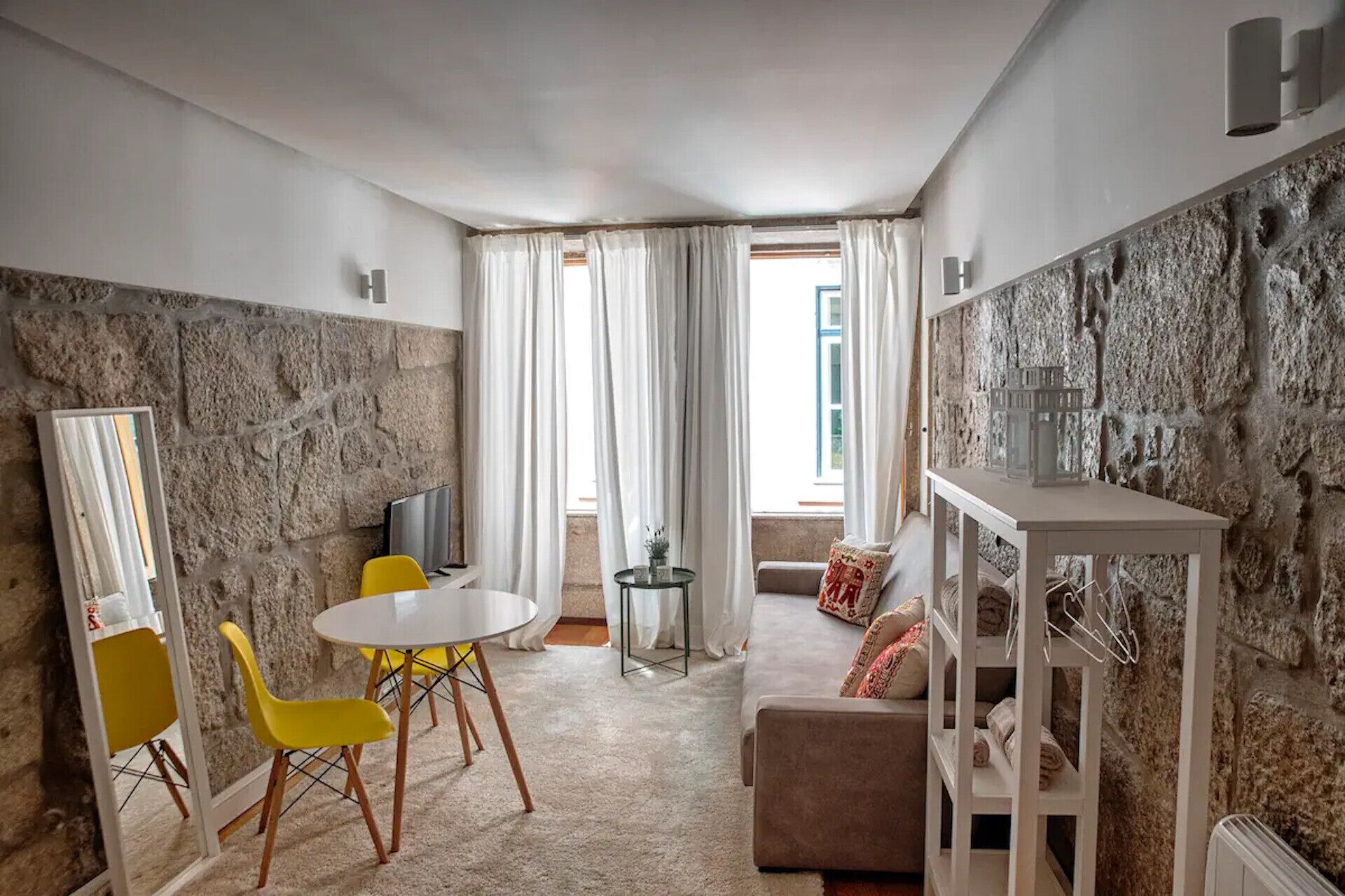 A modern living room with a stone wall, a round table with yellow chairs, a sofa, and a TV.