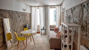 A modern living room with a stone wall, a round table with yellow chairs, a sofa, and a TV. - Try Oporto Ribeira - Caves Port-Wine (Oporto)