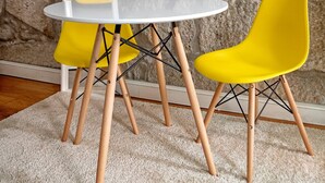 A room with a stone wall, a round white table, and two yellow chairs with wooden legs. - Try Oporto Ribeira - Caves Port-Wine (Oporto)