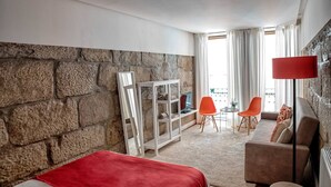 A hotel room with a stone wall, a bed with a red blanket, a sofa, two orange chairs, a small table, and a floor lamp. - Try Oporto Ribeira - Barco Rabelo (Oporto)