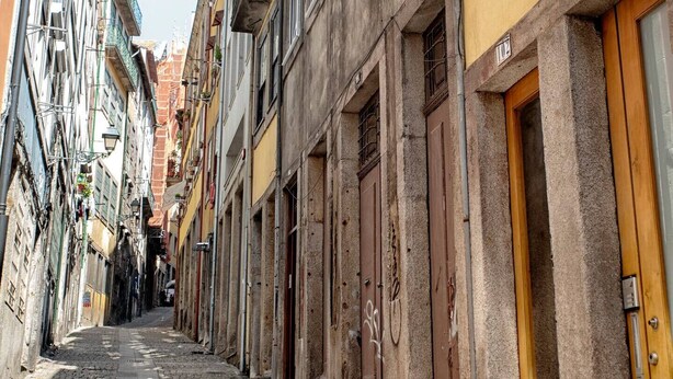 A narrow cobblestone street lined with historic buildings, featuring balconies, wooden doors, and numbered windows. - Try Oporto Ribeira - Barco Rabelo (Oporto)