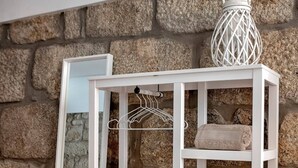 A white wooden shelf unit with towels and a hanging light fixture against a stone wall. - Try Oporto Ribeira - Barco Rabelo (Oporto)
