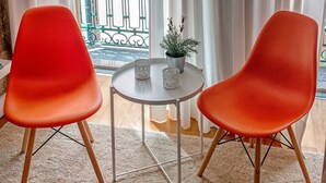 A room with two red chairs, a small round table, and a view of a balcony with a metal gate and a potted plant. - Try Oporto Ribeira - Barco Rabelo (Oporto)