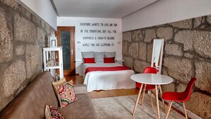 A modern bedroom with a stone wall, a bed with red and white bedding, a small table with red chairs, and a motivational quote on the wall. - Try Oporto Ribeira - Rio Douro (Oporto)