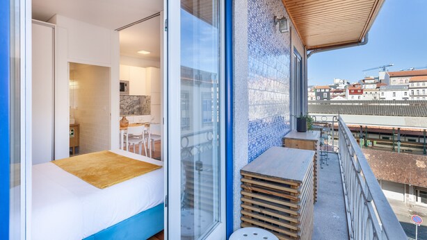 A modern room with a bed, a small table, and a view of the cityscape through large windows. - D&S - Porto São Bento Apartments III (Oporto)
