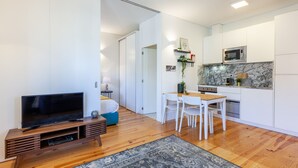 A modern living room with a flat-screen TV, wooden entertainment unit, and a dining area with a table and chairs. - D&S - Porto São Bento Apartments III (Oporto)