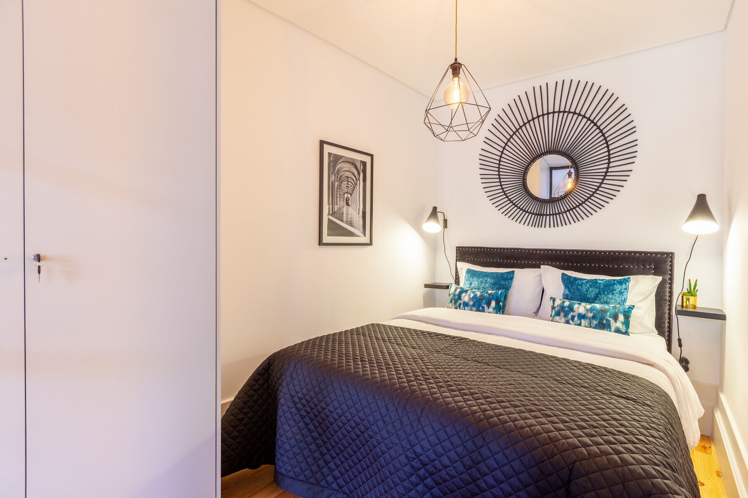 A bedroom with a bed, a wall-mounted mirror, and a picture.