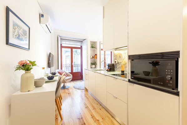 Une cuisine moderne avec des meubles blancs, un four encastré et un coin repas comprenant une chaise et une table.