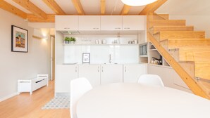 Una cocina moderna con armarios blancos, una escalera de madera y un comedor con una mesa y sillas blancas.