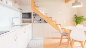 Una cocina moderna con armarios blancos, una escalera de madera y un comedor con sillas blancas.