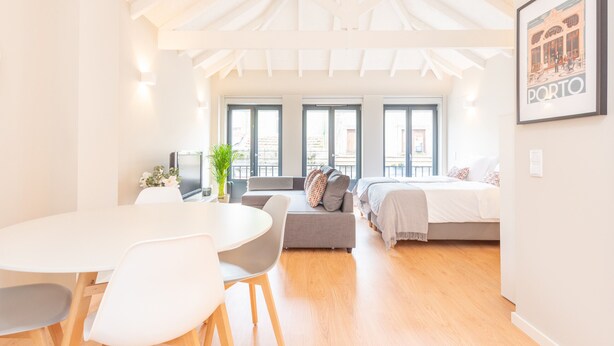 A bright, open-plan living space with a dining area, a sofa, a bed, and large windows. - 12 Sweet Caroline 2 (Oporto)