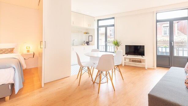 Una habitación moderna y luminosa con cama, un comedor con sillas y mesa, televisor y un amplio ventanal con vistas al exterior.
