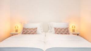 A double bed with white bedding and two decorative pillows, flanked by bedside tables with lamps.
