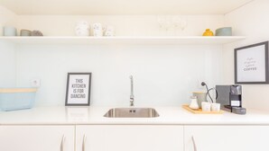 Una cocina moderna con un lavamanos de acero inoxidable, armarios blancos y una cafetera sobre la encimera.