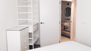 A bedroom with a white dresser, a built-in closet with shelves, and a bathroom with a sink and mirror. - Ático con Terraza 3.1 (Pontevedra)
