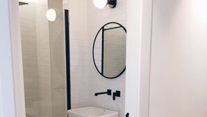 A modern bathroom with a glass shower enclosure, a white sink, and a mirror on the wall. - Ático con Terraza 3.1 (Pontevedra)