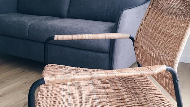 A wicker chair with a black metal frame, positioned in front of a dark grey sofa. - Loft con Terraza 3.2 (Pontevedra)