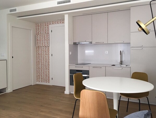 A modern kitchen with stainless steel appliances, a white dining table, and two chairs.