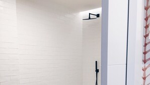 A modern bathroom with white subway tiles, a shower with a handheld showerhead, and a toilet with a safety grab bar. - Loft con Terraza 3.2 (Pontevedra)