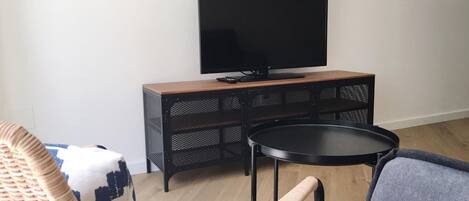 A living room with a television on a wooden cabinet, a round table, and two wicker chairs.