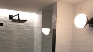 Une salle de bain moderne avec une douche à l’italienne en verre, un lavabo blanc doté d’un plan de toilette en bois et deux appliques murales.