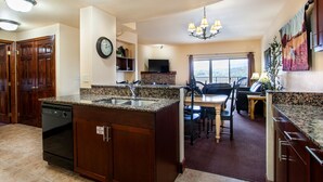 A kitchen with granite countertops, a dishwasher, a dining area with a table and chairs, a chandelier, and a large window. - The Bear Paw Palace - Mtn View & Community Pools! (Pigeon Forge)