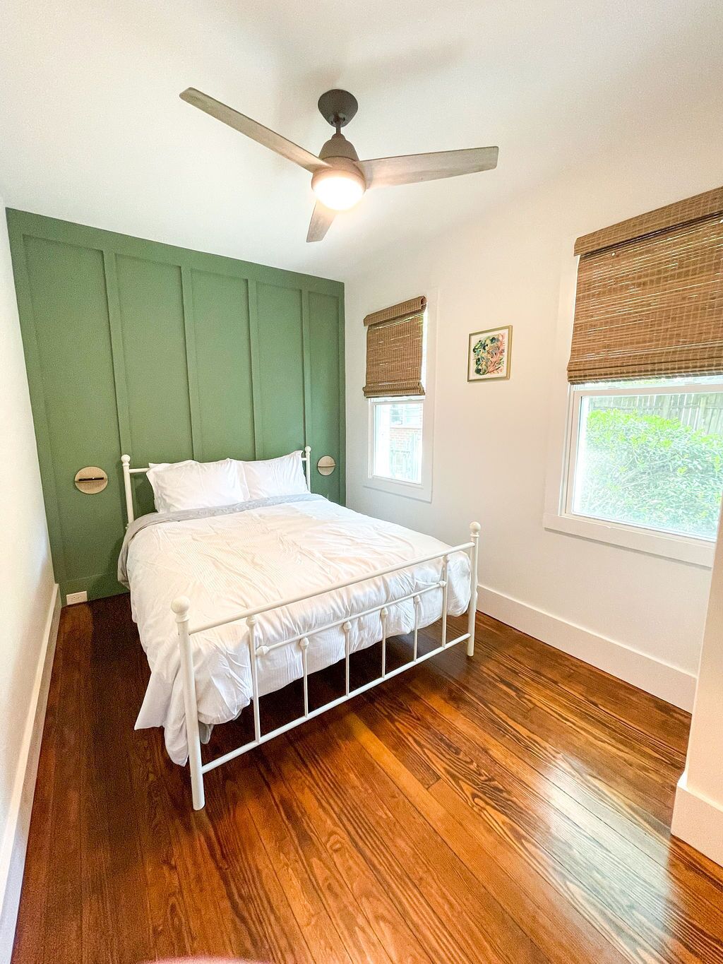 A bedroom with a bed, a ceiling fan, a window with blinds, and a small picture on the wall.