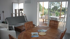 A modern living room with a wooden dining table, a sofa, and a sliding glass door leading to an outdoor patio.