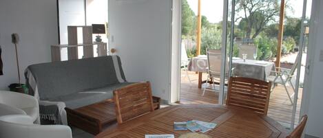 Una sala moderna con una mesa de comedor de madera, un sofá y un ventanal corredizo que da a un patio exterior.