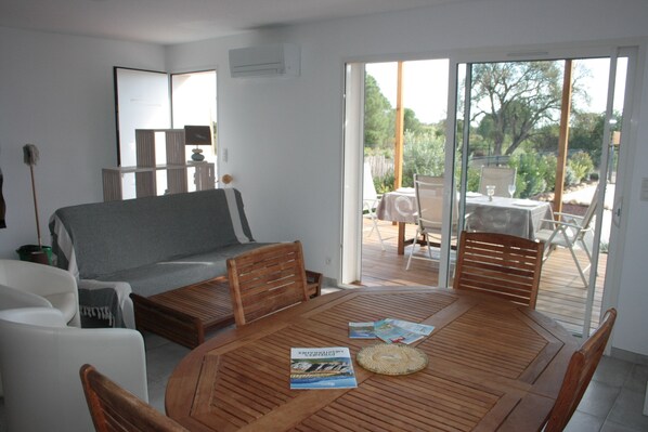 A modern living room with a wooden dining table, a sofa, and a sliding glass door leading to an outdoor patio.