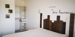 A bedroom with a white bed, a wooden headboard, and a closet with hanging space.