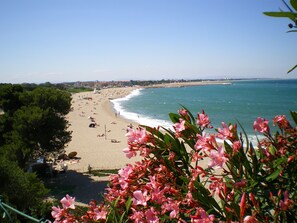 Una playa con gente tomando el sol y nadando, rodeada de vegetación y con vistas al mar.