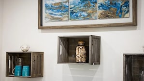Una habitación con un armario de madera que contiene un objeto decorativo, una obra de arte enmarcada encima y un objeto azul en el suelo.