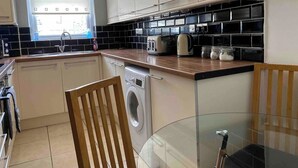Une cuisine de taille réduite, équipée d’un lave-linge, d’une table en verre et d’une fenêtre avec des stores.