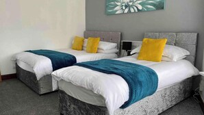Deux lits jumeaux avec des têtes de lit grises et une literie blanche, chacun agrémenté d’un coussin jaune et d’un plaid turquoise.