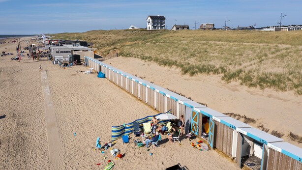 Un parque de caravanas frente a la playa, con varias caravanas y tiendas de campaña, una playa arenosa y una zona de dunas cubierta de césped al fondo.