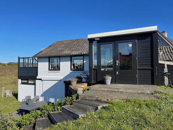 A modern house with a white exterior, a dark door, and a small porch with steps leading to a seating area.