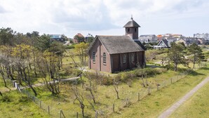 Una pequeña iglesia de ladrillo con un campanario, rodeada por un área cercada con árboles y un sendero.