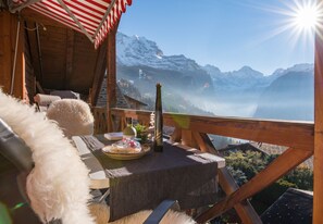 A wooden deck with a table set for dining, overlooking a mountainous landscape with snow-capped peaks. - Chalet Rose Penthouse Residence (Wengen)